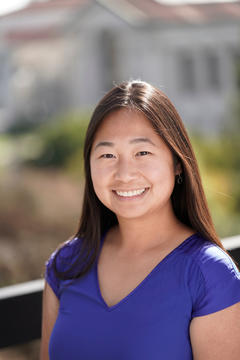 a woman in a blue v neck shirt stands in front of a dark fence with a blurry background