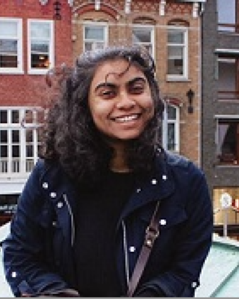 Woman with wind blown hair stands on a rooftop with three brick buildings in the background